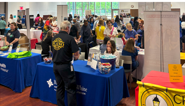 Several tables with health and wellness representatives and crowds of people