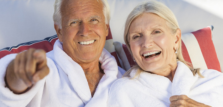 A couple sitting next to each other wearing bathrobes and colorful pillows behind them