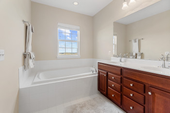 Bathroom with soaking tub ,dual sinks, vanity with extensive cabinet space, tile floors, and tiled bath