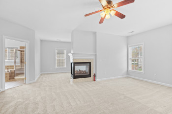 Unfurnished living room with light colored carpet, ceiling fan, and a multi sided fireplace
