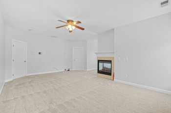 Unfurnished living room featuring light colored carpet, ceiling fan, and a multi sided fireplace