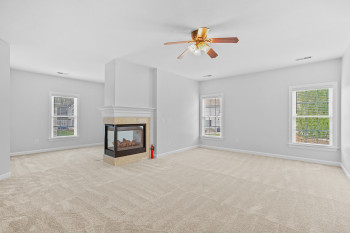 Unfurnished living room featuring light colored carpet, ceiling fan, and a tiled fireplace