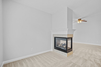 Unfurnished living room featuring light carpet, ceiling fan, and a multi sided fireplace