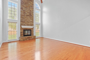 Unfurnished living room featuring a healthy amount of sunlight, a towering ceiling, light wood-type flooring, and a stone fireplace
