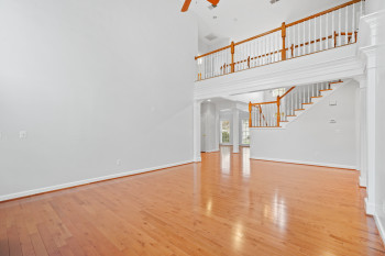 Unfurnished living room featuring ceiling fan, a towering ceiling, light hardwood / wood-style floors, and decorative columns