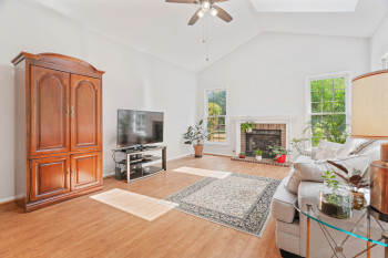 Living room with ceiling fan, light hardwood / wood-style flooring, a brick fireplace, and high vaulted ceiling