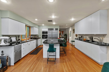Kitchen featuring appliances with stainless steel finishes, dark countertops, a kitchen breakfast bar, light wood finished floors, and white cabinets