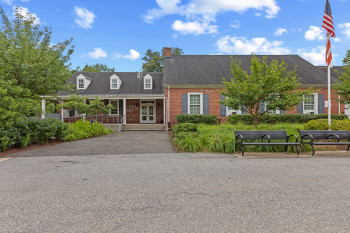 View of front of home with brick siding, a chimney, a porch, french doors, and a shingled roof