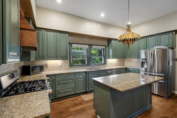 Kitchen with appliances with stainless steel finishes, green cabinetry, light stone counters, wood finished floors, and recessed lighting