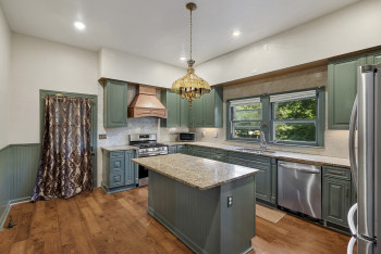 Kitchen with custom exhaust hood, stainless steel appliances, green cabinetry, a kitchen island, and light stone counters