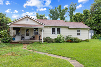 View of front of house with a front lawn, covered porch, and roof with shingles