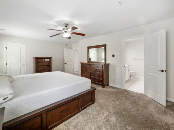 Bedroom with light carpet, connected bathroom, and a ceiling fan