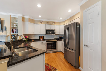 Kitchen featuring dark stone countertops, appliances with stainless steel finishes, decorative backsplash, light wood-style floors, and white cabinetry