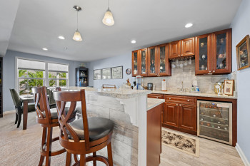 Indoor wet bar featuring decorative backsplash, beverage cooler, glass insert cabinets, decorative light fixtures, and upscale cabinets