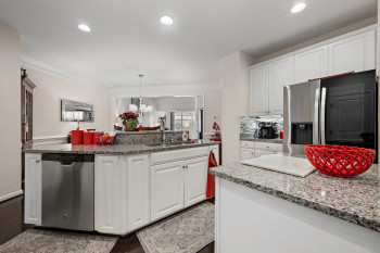 Kitchen with white cabinetry, appliances with stainless steel finishes, dark stone countertops, decorative light fixtures, and tasteful backsplash