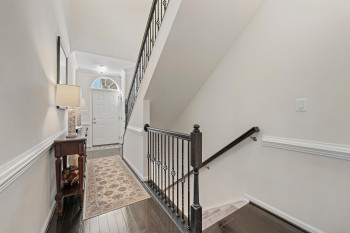 Stairway to lower level with hardwood floored hallway and wrought iron balusters in railing