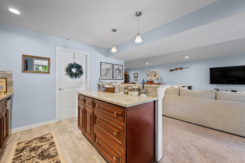Alternate view of bar/kitchen area with recessed lighting, light stone counters, hanging light fixtures,  and open floor plan