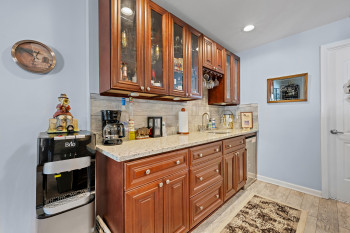 Bar area featuring tasteful backsplash, light wood-style flooring, brown cabinetry, light stone counters, and glass insert cabinets