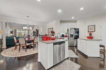 Kitchen featuring 2 islands with sink, light stone counters, a kitchen bar, white cabinetry, and decorative columns