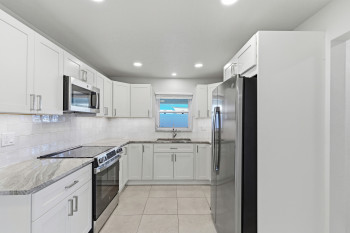 Kitchen with stainless steel appliances, light Quartz countertops, white shaker cabinetry, light tile patterned floors, and recessed lighting
