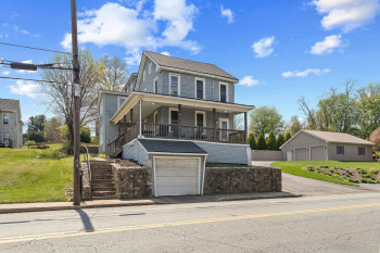 View of front of property featuring covered porch, a front yard, a shingled roof, and an attached garage