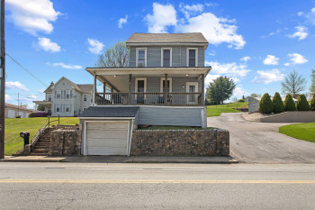 View of front of home featuring covered porch, an attached garage, a shingled roof, driveway, and a front lawn