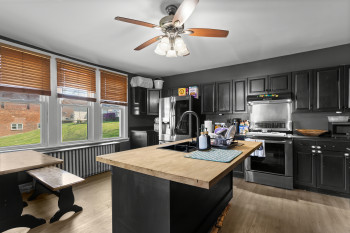 Kitchen featuring dark cabinetry, stainless steel appliances, a kitchen island with sink, a ceiling fan, and butcher block countertops