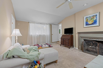Carpeted room featuring a fireplace with a decorative screen, a vaulted ceiling, and a ceiling fan
