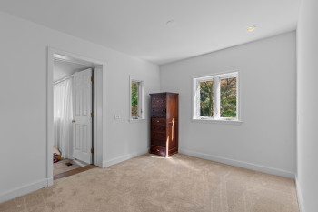 Neutral-toned carpet flooring and bright white walls define this room, featuring recessed lighting and two white-framed windows