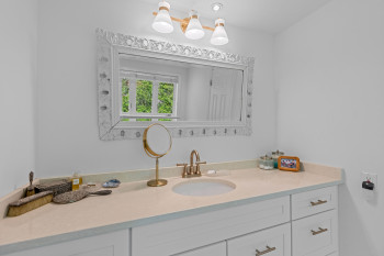 White vanity with a single integrated sink and bronze-finish hardware, illuminated by a three-light fixture