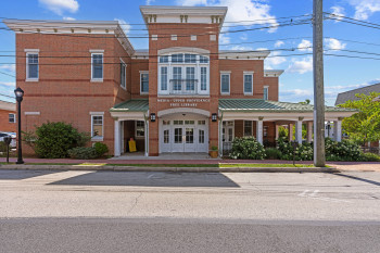 Brick facade building featuring a central entrance with double doors, a second-story balcony, and a covered porch with white columns