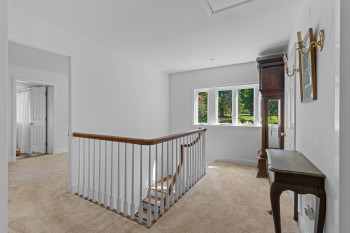 Carpeted hallway featuring a white spindle railing with a wood-finish handrail, multiple white-framed windows, and a white paneled door