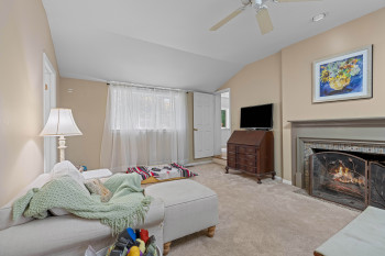 Carpeted living space featuring a fireplace with decorative screen, an angled ceiling, a ceiling fan, and a window with sheer curtains