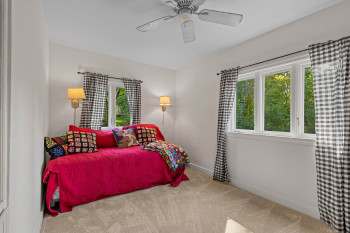 Carpeted room with a ceiling fan, dual windows, and wall-mounted sconces