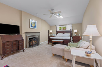 Carpeted room featuring a built-in fireplace with a stone surround and mantel, a vaulted ceiling, a skylight, a ceiling fan, and a window with white trim