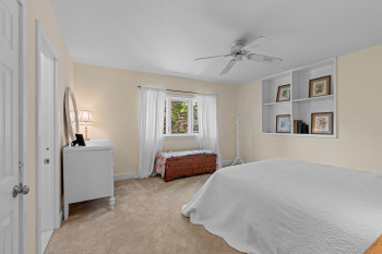 Carpeted room featuring a ceiling fan with integrated lighting, a window with white sheer curtains, and built-in shelving