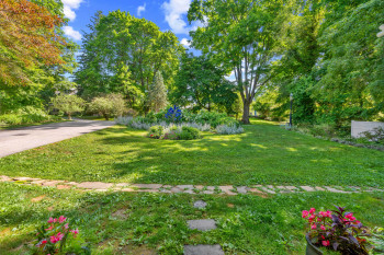 Expansive front lawn featuring a landscaped garden bed, mature trees, and a paved driveway