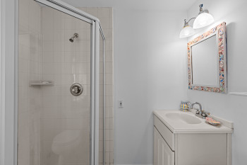 White tile shower with glass enclosure, single vanity with integrated sink, chrome faucet, and decorative framed mirror