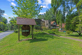 Stone and wood-sided building featuring multiple gabled roofs, natural stone facade, and extensive surrounding greenery