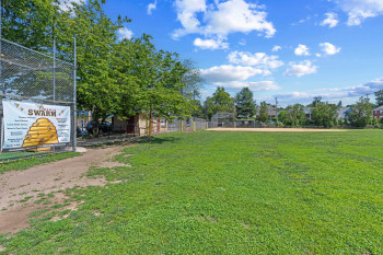 Expansive green space featuring a large grass field, perimeter fencing, and mature trees