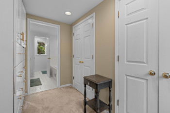 Hallway with carpet flooring, recessed lighting, and a neutral wall color, featuring multiple panel doors with brass hardware, and a built-in white cabinetry unit with gold-toned pulls