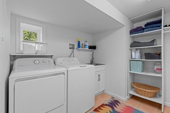 Dedicated laundry area featuring a white dryer and top-loading washing machine, a utility sink with a cabinet, and a wall-mounted shelving unit