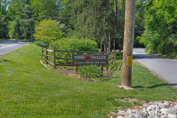 Rose Valley community sign surrounded by lush greenery and bordered by a rustic wooden fence