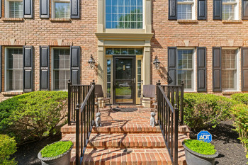 Brick exterior featuring a portico entry with a glass storm door, black shutters, and decorative outdoor lighting