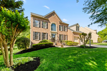 Brick exterior featuring black shutters, an arched transom window, a two-car garage, manicured landscaping, and a sloped front lawn