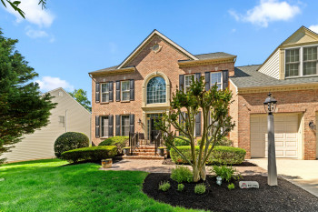 Brick facade residence featuring a prominent arched window, dark shutters, and a well-maintained lawn