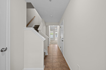 Entryway featuring neutral wall paint, terracotta-toned tile flooring, and a staircase with carpeted treads and a wooden handrail