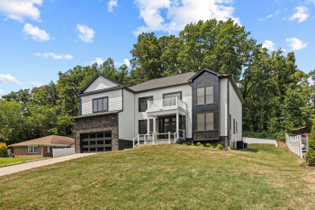 Modern exterior with white siding, dark stone accents, and a prominent balcony