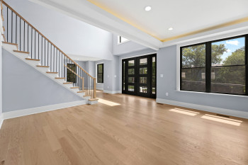 Hardwood-style flooring throughout, dual entry doors with multiple glass panes, black window frames, recessed ceiling lighting, and a prominent staircase with wood handrails and black balusters