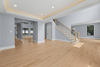 Light wood-finish flooring, recessed lighting, tray ceiling with cove lighting, and a staircase with wood treads and black metal balusters
